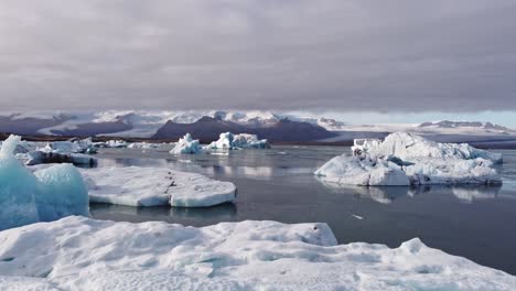 aerial shot showcases icebergs of various sizes and shades of blue and white, densely packed within the vast jökulsárlón glacier lagoon, with a backdrop of rugged, snow-capped mountains