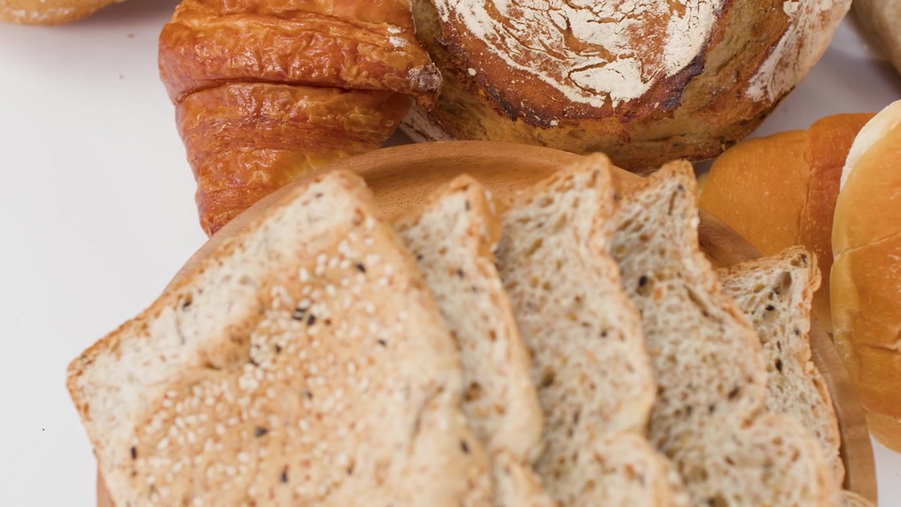 Sakte kamerarotasjon rundt et utvalg av håndverksbrød, croissanter og skivet fullkornstoast
