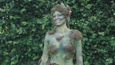 Medium-shot-of-a-female-model-laughing-wearing-green-bodypaint-watching-forwards-in-a-forest,-in-the-style-of-nature-inspired-forms