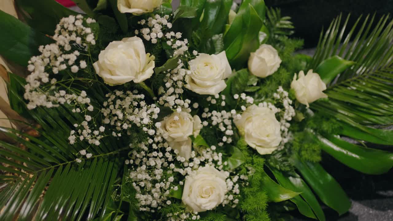 Buquê elegante de rosas brancas e gipsofilas com folhagem tropical exuberante em iluminação suave.