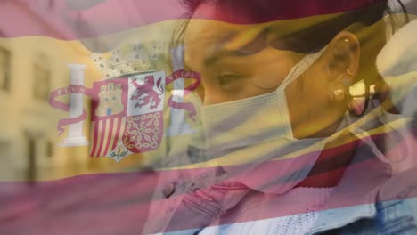 animation of flag of spain waving over african american woman wearing face mask in city street