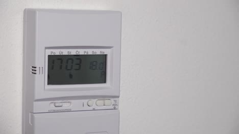 Setting-lower-heating-temperature-on-digital-thermostat,-hand-closeup-view,-saving-costs