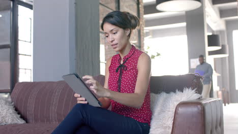 in a business setting, a young biracial woman is using a tablet on a sofa