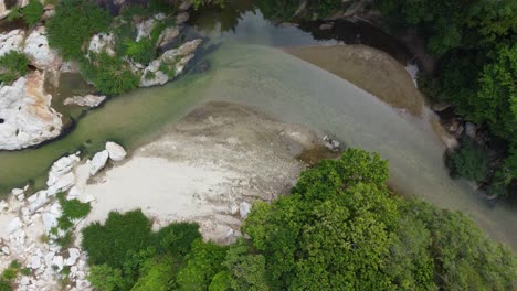 Aerial-top-down-pan-follows-vibrant-green-waters-of-river-in-valley-of-Santa-Marta,-Magdalena,-Colombia