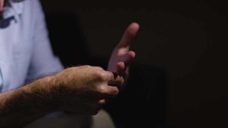 Close Up Of Depressed Divorced Mature Man Sitting In Darkness Holding Wedding Ring With Low Key Lighting