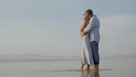 feliz pareja caucásica con gafas de sol viendo la puesta de sol en la orilla del mar