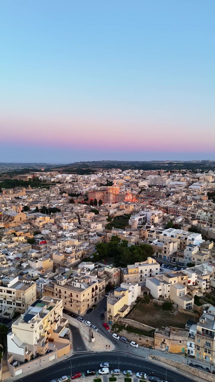 Rabat, Malta: Sankt Pauls Basilika og dekorerede gader i den gamle bydel under en landsbyfest i skumringen, med kirkekuppel, stenbygninger og bylys i et vertikalt luftfoto