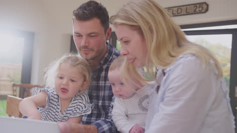 busy family kitchen with father working on laptop with daughter and mother holding baby son - shot in slow motion