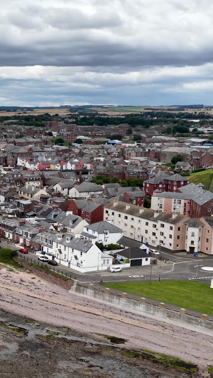 La telecamera del drone effettua una panoramica sopra Dundee, rivelando la città, la costa rocciosa, i campi erbosi e il cielo coperto.