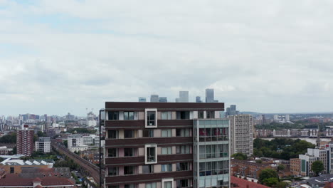 Vista-Panorámica-Aérea-Del-Distrito-De-La-Ciudad-En-Thames-Rive-Bank-Y-Rascacielos-En-El-Centro-Financiero-Canary-Wharf.-Escondiéndose-Gradualmente-Detrás-Del-Edificio-De-Apartamentos.-Londres,-Reino-Unido