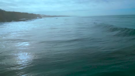 drone shot of two pelicans flying with the waves on the carlsbad coastline on a cloudy day