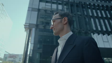 elegant handsome caucasian man in suit and glasses outdoors looking aside at camera, orbital low angle shot