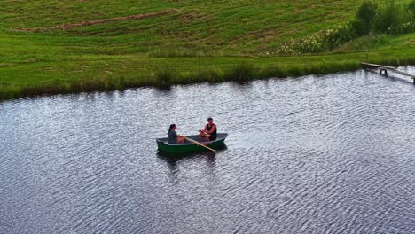 slow motion orbit aerial of couple peacefully rowing a boat across pond