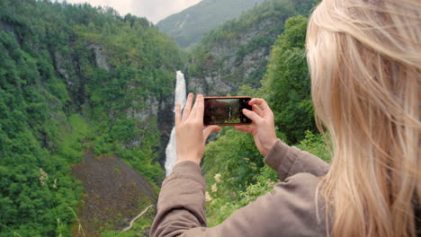 mujer tomando una foto de una cascada en noruega