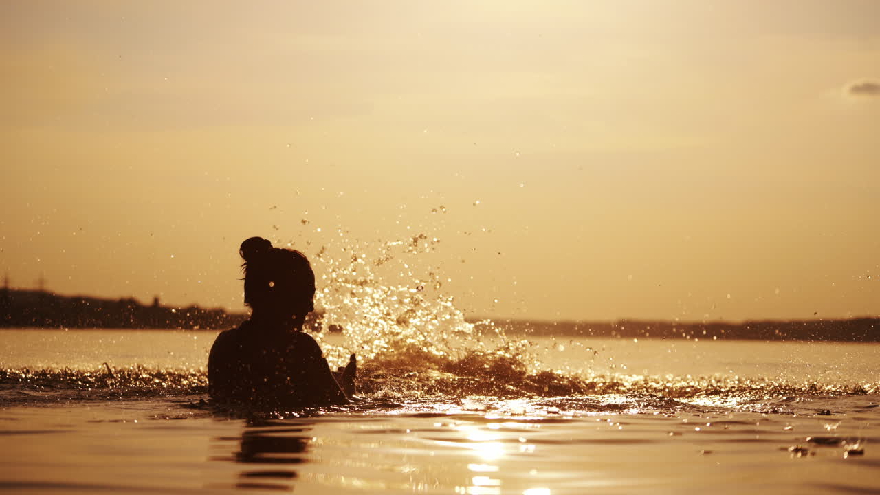 Mother and boy inside the river water at sunset. Silhouette of a woman throwing a boy up into the evening water. Happy family holidays outdoors.