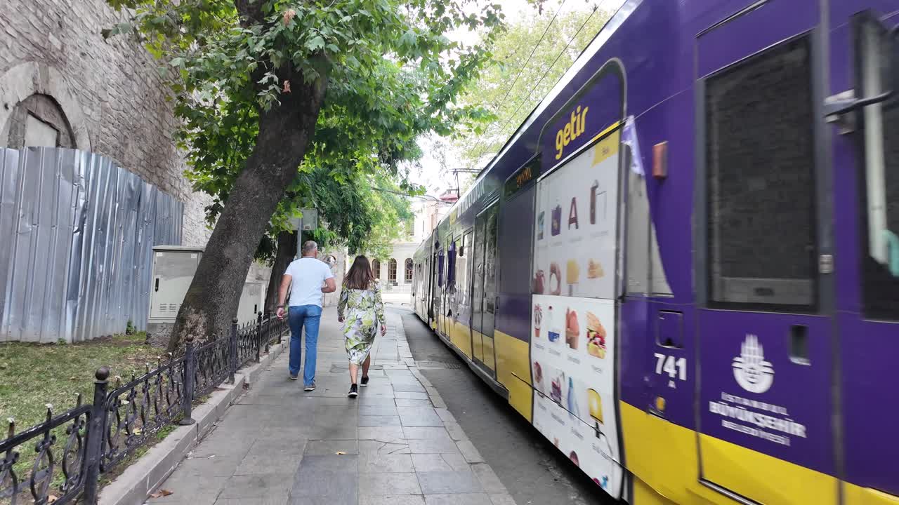 Persone camminano sul marciapiede mentre un tram viola passa a Istanbul