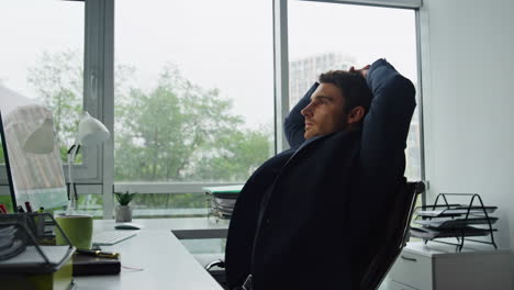 office worker leaning chair at glass workplace. thoughtful man taking break