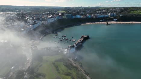 Aerial-shot-approaching-the-coast-of-Tenby,-Wales,-with-fog-enveloping-coast