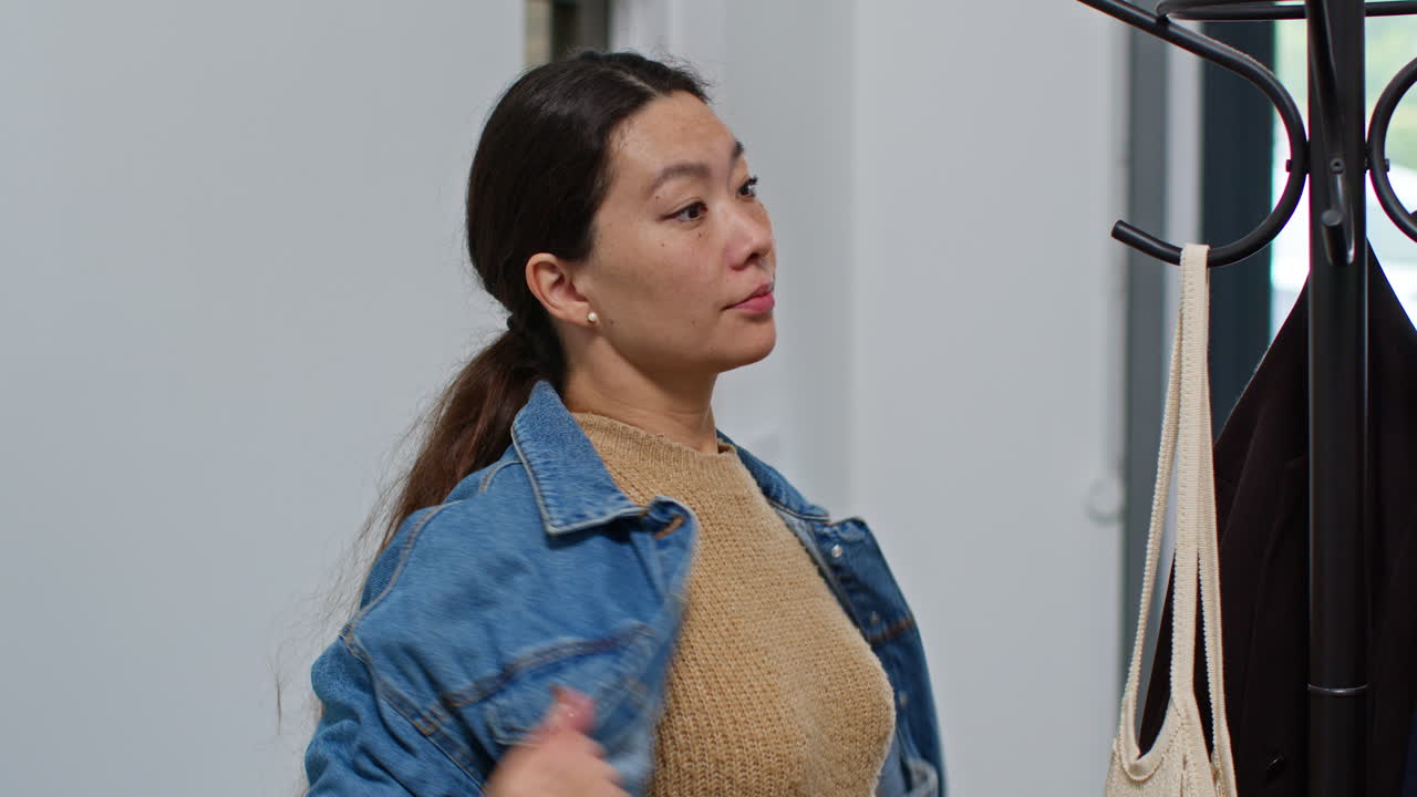 쇼핑에서 돌아온 여자가 가방을 집으로 들고 들어가기 전에 코트를 스탠드에 매달고 있습니다.