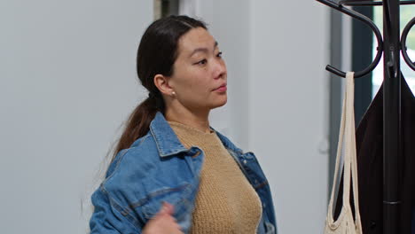 쇼핑에서 돌아온 여자가 가방을 집으로 들고 들어가기 전에 코트를 스탠드에 매달고 있습니다.