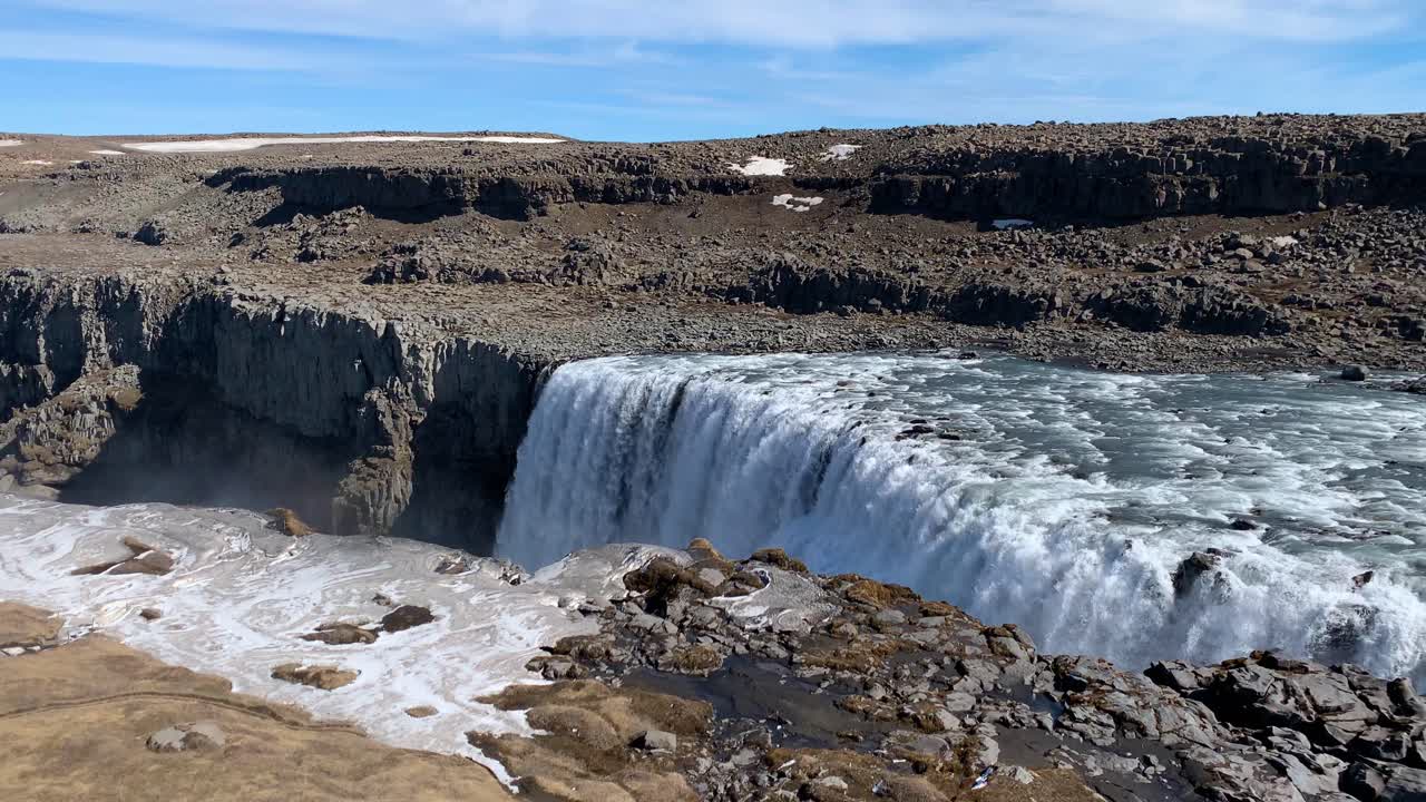 The dry and rocky Icelandic landscape around Dettifoss, wich is one of the most powerful waterfalls in Europe, on a sunny day with a beautiful rainbow appearing in the sky