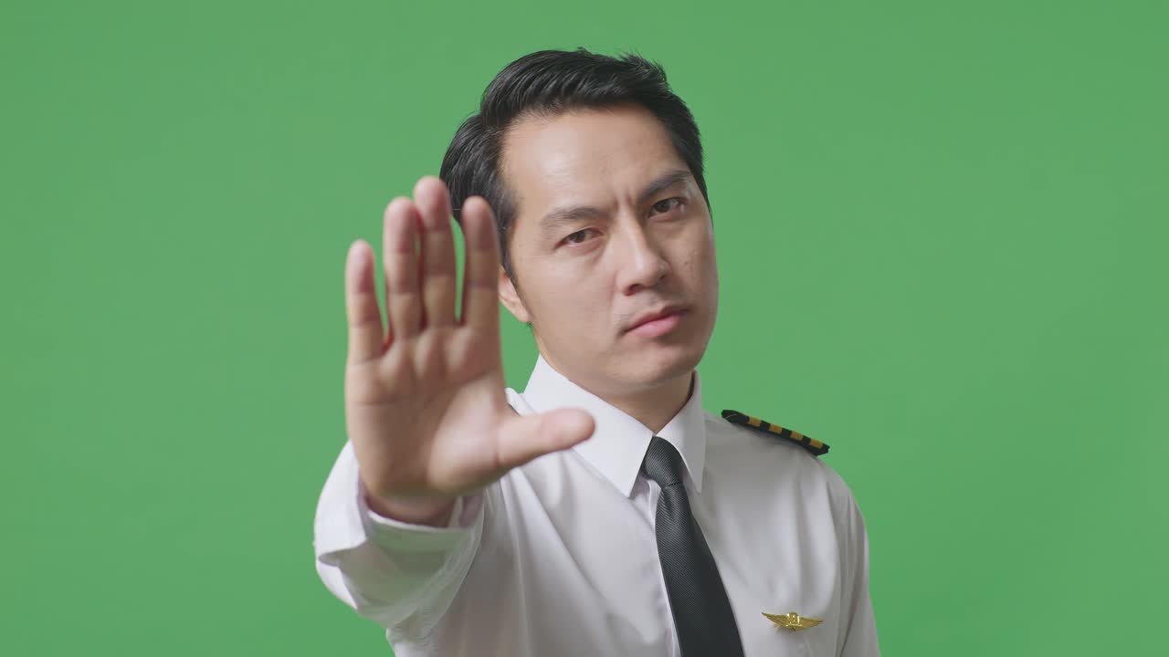 동양인 조종사가 카메라를 바라보고 녹색 스크린 배경 스튜디오에서 손 표시 없이 불쾌감을 표합니다.