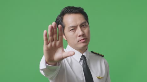 close up of asian man pilot looking at camera and disapproving with no hand sign in the green screen background studio