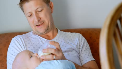 padre alimentando leche a su bebé en la sala de estar 4k
