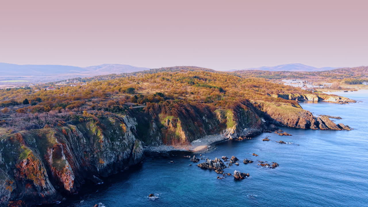 Cliffs lined with autumn coastal colors. Vibrant seasonal hues cover rugged headlands above calm blue coastal waters