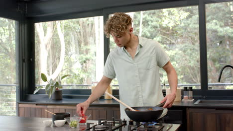 young man cooking in modern kitchen, adding ingredients to sizzling pan