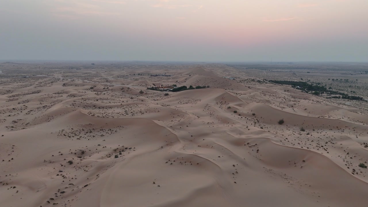 Sunset over desert sand dunes with palm oasis and rolling landscape in Abu Dhabi, aerial tracking left