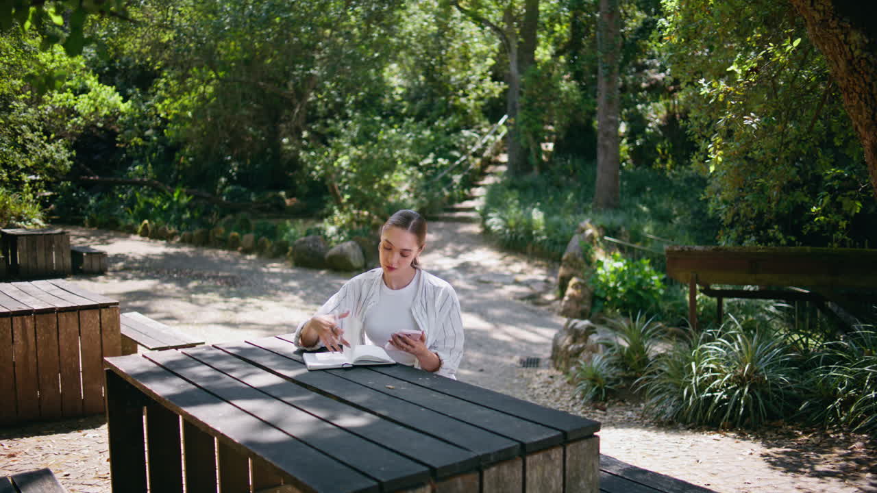 스마트폰을 사용하는 소녀 복사 책 온라인 서핑 정보 앉아 공원 테이블.