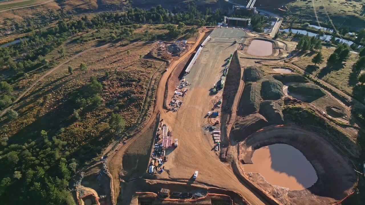 Aerial view of a highway construction area in Canberra, showcasing exposed structural foundations and a nearby dam supplying water to the site.