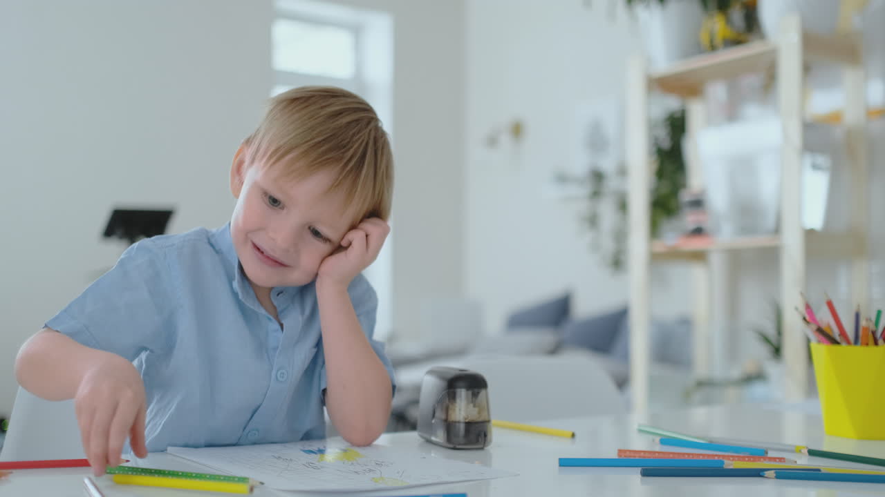A small child sitting at the table draws a pencil drawing painting in different colors