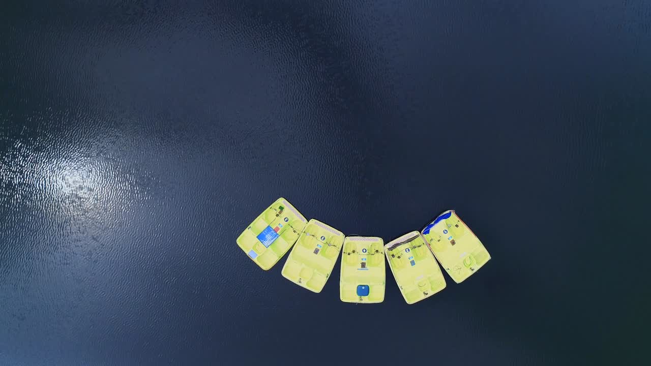 Looping aerial view of a few paddeleboats floating on lake in the scenic background. 4K.