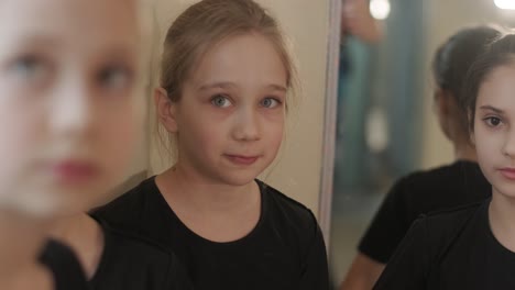 a group of young ballet students in black dancewear practicing positions in a spacious ballet studio with wooden flooring and wall-mounted barres. focused expressions and synchronized movements.