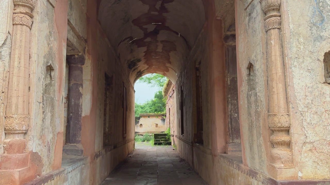 Camera tilts down from the detailed carvings of an old fort entrance to reveal a long arched passage leading outside, showing historic architecture
