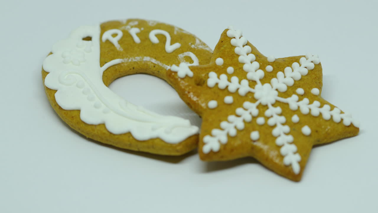 A hand lays a confectionery gingerbread with white decoration on top in the shape of a star and horseshoe wirh PF on a white background