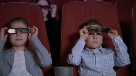 children wearing 3d glasses at cinema chair. brother and sister watch 3d film