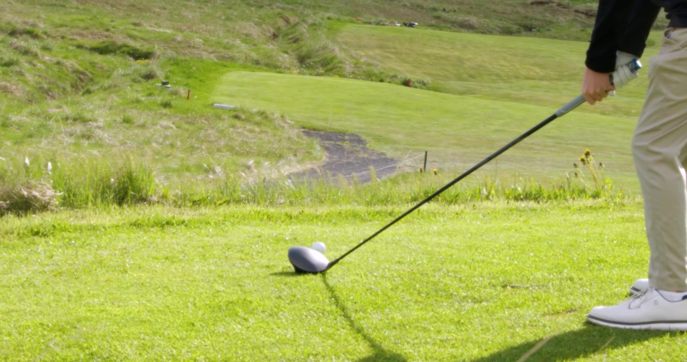 Una persona che indossa un guanto e scarpe da golf si prepara a colpire una pallina da golf con un driver su una bellissima area di partenza di un campo da golf verde.