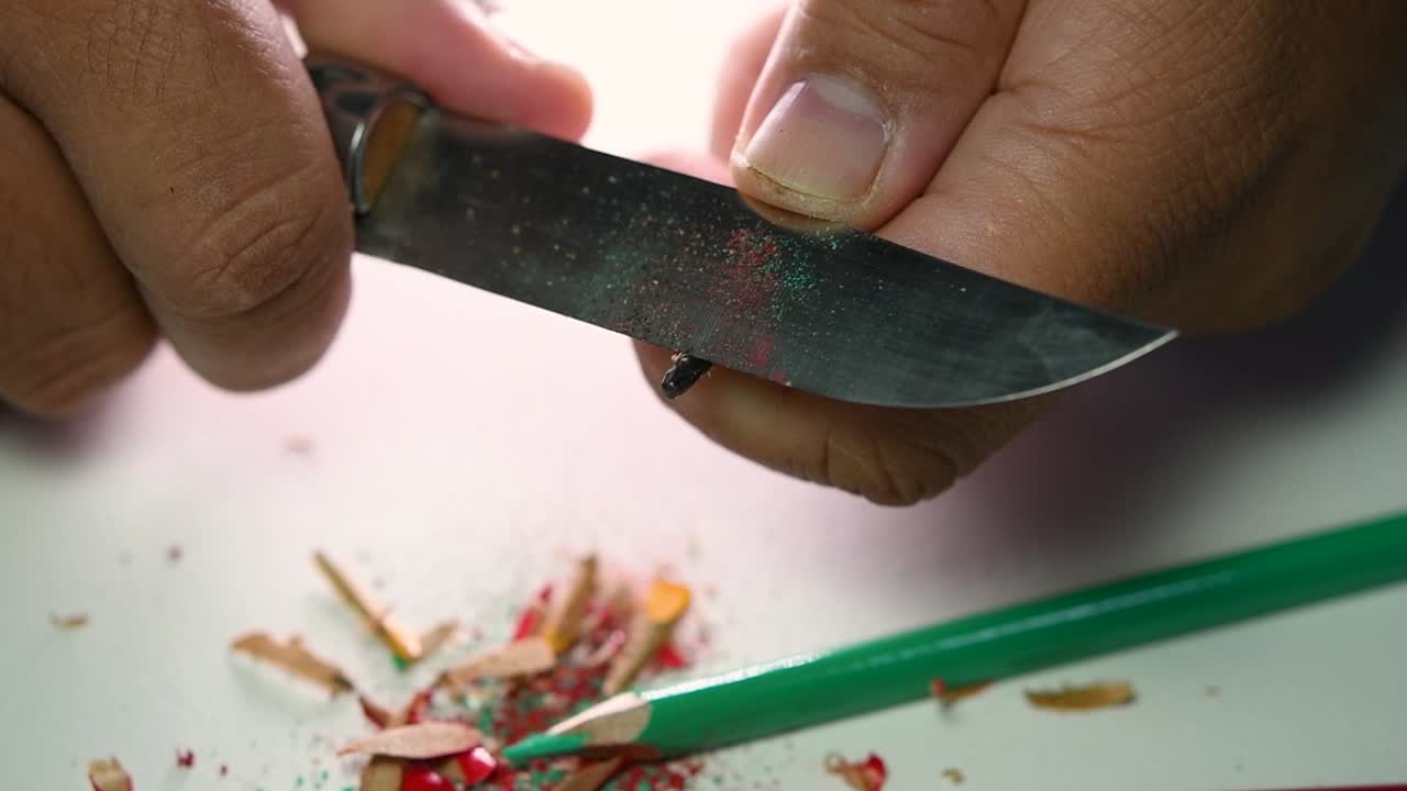 날카로운 칼로 연필과 색연필을 천천히 갈고 있는 손의 영상