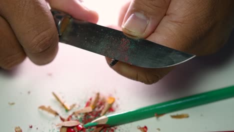 imágenes de manos afilando lentamente un lápiz y algunos lápices de colores con un cuchillo afilado