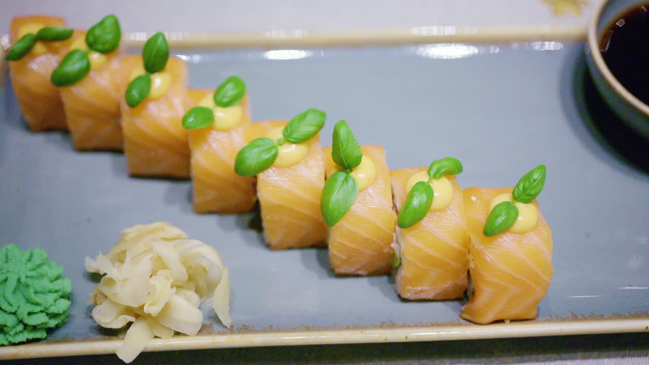 Un piatto di sushi di salmone, presentato ordinatamente con guarnizione verde sopra, con salsa di soia in una ciotolina, più wasabi e zenzero marinato a lato.