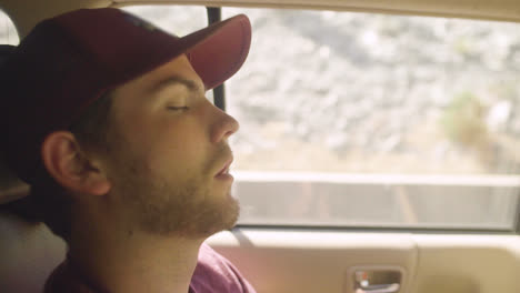 attractive young tired white man gen z millennial falls asleep in the back of car with mouth open during a road trip van life adventure in slow motion