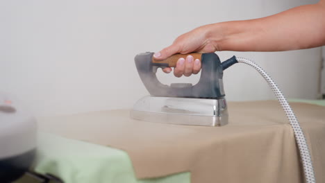 clothing designer moving pressing iron on cotton material, placing it on protective pad, focusing on precise heat application, ensuring crisp finish, controlling steam for polished garment