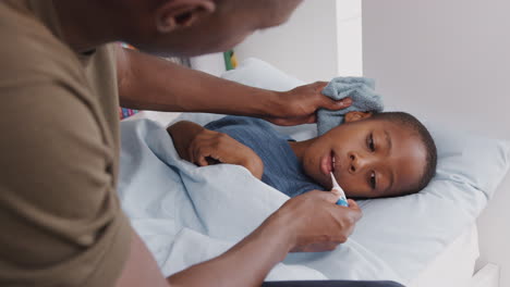father caring for sick son ill in bed taking temperature with thermometer
