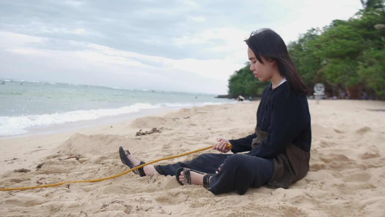Side View of Pensive Young Woman Holding Rope on Windy Beach, Symbolizing Inner Turmoil. -static shot