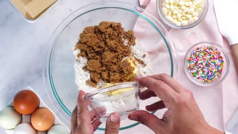 baking confetti sugar cookies and using a white electric mixer and adding brown sugar to the batter. in the kitchen making a dessert. making cookies with a white background, pink napkin and eggs