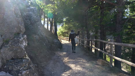 Traveler-walking-along-path-surrounded-by-pine-trees-at-sunset