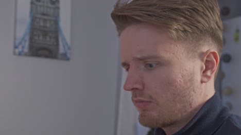 a close-up of a skeptical young man as he sits down at his desk trying to understand what has just appeared on his computer screen